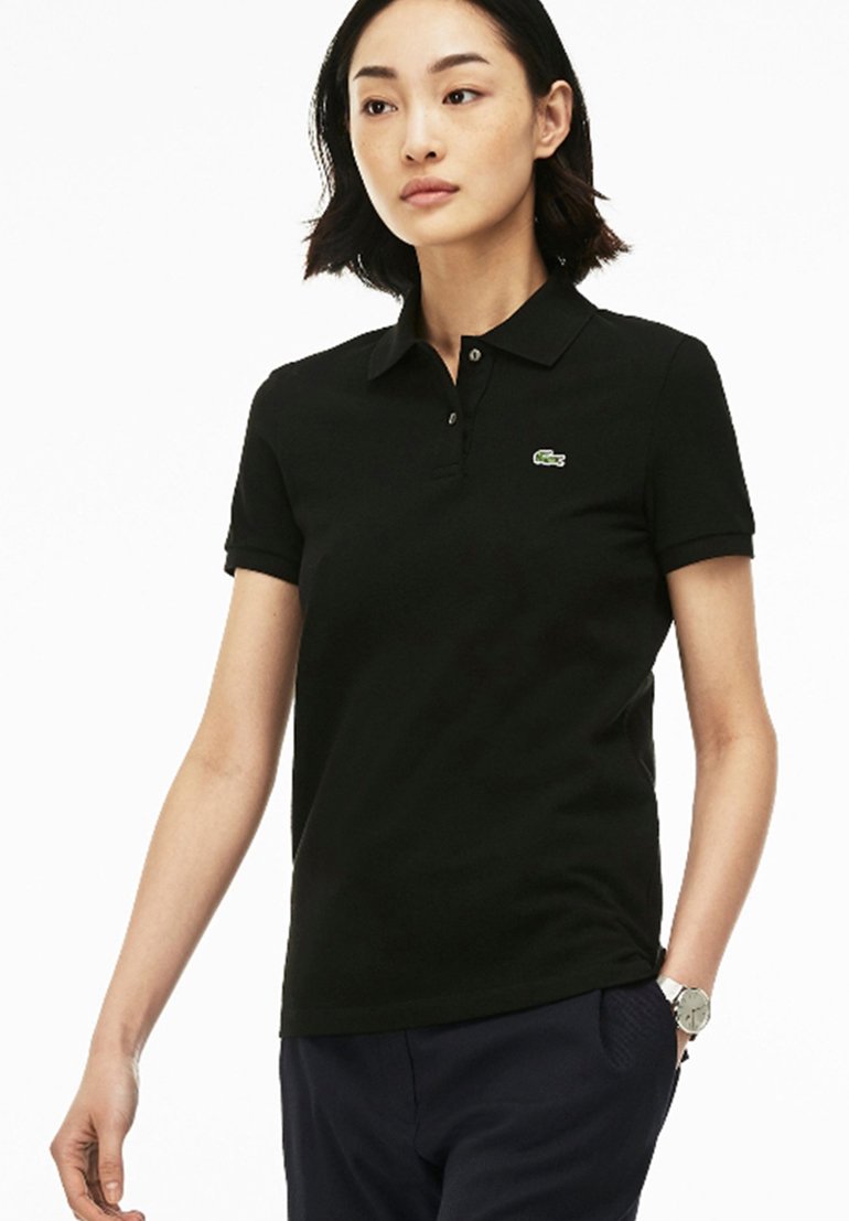 Svart polo skjorta med krage, korta ärmar och en grön Lacoste-logotyp på bröstet. Slät yta, kroppsnära design, enfärgad.