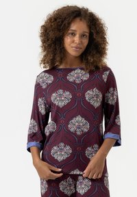 Bordeaux top met bloemig patroon in wit, blauw en rood. Heeft driekwartmouwen met blauwe manchetten en een ronde halslijn. Zachte textuur.