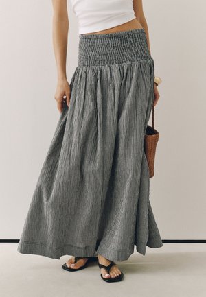 Kvinde iført en sort-hvid ternet maxi nederdel med høj talje, hvid cropped top, sorte sandaler og holder en brun flet taske.