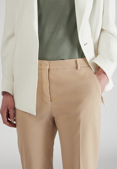 Lichte blazer in het wit, gecombineerd met een groene top en beige op maat gemaakte broeken. Opvallende texturen omvatten een gladde stof en subtiele stiksels.