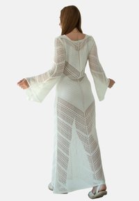 Długa biała sukienka szydełkowa z dzwonowymi rękawami, z diagonalnymi wzorami i otwartym tyłem. Lekka, teksturowana tkanina.