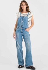 Blauwe denim salopettes met een losse pasvorm, voorzien van verstelbare banden, knopen aan de voorkant en zijzakken, gecombineerd met een gestreept top met korte mouwen.