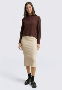 Brązowy, prążkowany sweter z długimi rękawami i wysokim kołnierzem, zestawiony z dopasowaną, beżową dzianinową spódnicą midi oraz czarnymi butami na platformie.