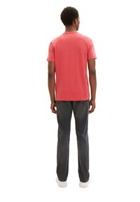 Rotes Baumwoll-T-Shirt mit Rundhalsausschnitt und kurzen Ärmeln, kombiniert mit dunkelgrauen Jeans, beides getragen mit weißen Sneakers.