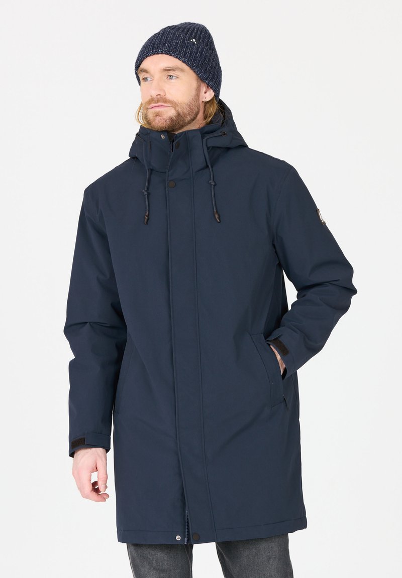 Parka impermeable azul marino con capucha, cordón y bolsillos laterales. Presenta una textura suave y se cierra con una cremallera y botones.