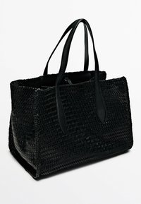 Sac fourre-tout noir en toile tissée avec des poignées en cuir lisse. Forme rectangulaire, intérieur spacieux, présentant une surface texturée et un design élégant.