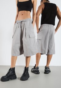 Shorts cargo gris avec une taille élastique et des poches des deux côtés. Le tissu est léger et lisse, associé à des bottes à plateforme noires.