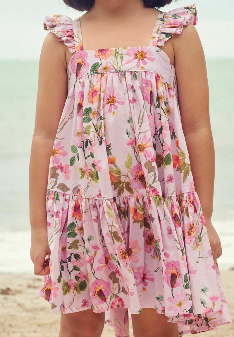 Robe florale rose avec des bretelles volantées, présentant un buste froncé et une jupe à volants. Le tissu affiche une variété de motifs floraux colorés.