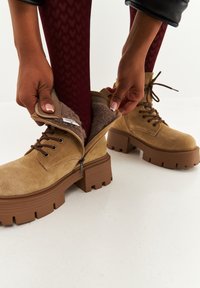Bordeaux suède enkellaarsjes met een stevige rubberen zool, met een ritssluiting en een zachte binnenvoering, die door een hand wordt open geritst.