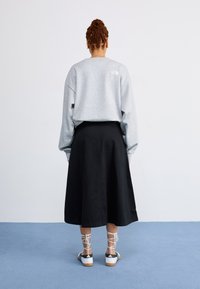 Felpa grigia oversize con spalle cadenti, abbinata a una gonna nera a trapezio. Sneakers bianche con strisce nere e lacci avvolti.