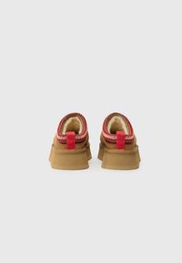 Brown footwear with a textured fabric upper, a red and patterned trim, and a thick cushioned sole; features a heel pull tab for easy wear.