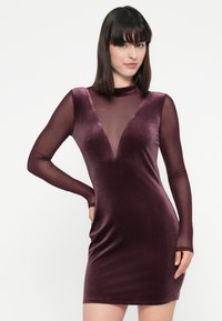 Velvet burgunderkjole med dyp V-hals, lange gjennomsiktige ermer og en tettsittende silhuett som fremhever en glatt tekstur og et elegant design.