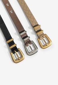 Trīs jostas: melna ar zelta sprādzi, brūna ar sudraba sprādzi un gaiši brūna ar zelta sprādzi. Redzamas dažādas strukturētas materiālu tekstūras.