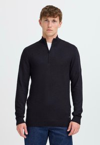 Pull à col zippé noir avec des manches longues et des poignets côtelés, fabriqué en matériau tricoté doux. Présente une texture lisse et une coupe ajustée.
