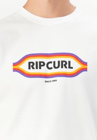 Hvid bomulds t-shirt med et markant sort "RIP CURL" logo, omkranset af bølgende linjer i rød, orange og lilla, med "SINCE 1969" under.