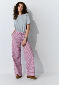 Grijze T-shirt met korte mouwen gecombineerd met rode en witte geblokte wijde broek. De outfit heeft een trekkoord in de taille en bruine schoenen.