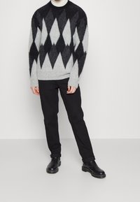 Grå och svart argyle-tröja gjord av ett mjukt, luddigt material; kombinerad med svarta byxor och svarta, polerade ankelstövlar.