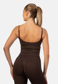 Top de tirantes marrón y leggins a juego; ambos presentan un ajuste ceñido y tirantes ajustables. La textura parece suave con un ligero brillo.