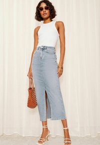 Licht gewassen denim maxi rok met een zijsplit, hoge taille en een gladde textuur. Gecombineerd met een witte tanktop en gestrikte witte hakschoenen.