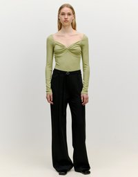 Langärmliges, olivgrünes Oberteil mit gedrehtem Vorderteil, kombiniert mit hoch taillierten, weit geschnittenen schwarzen Hosen und eleganten schwarzen Schuhen.