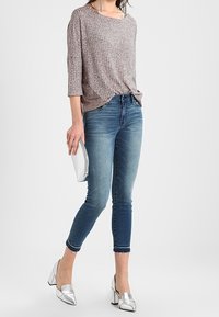 Ljust brunt, texturerat stickat linne med 3/4 ärmar, kombinerat med blå jeans i skinny-fit och silverfärgade klackskor. Accessoar: liten silverfärgad kuvertväska.