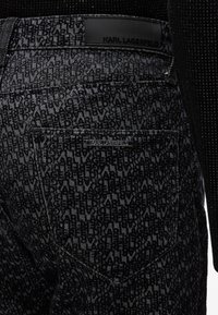 Zwarte jeans met een reliëflogo-patroon, subtiele glans, een merkembleem op de achterkant en een standaard zakontwerp.