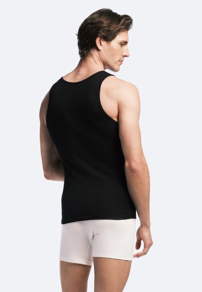 Débardeur en coton noir avec une texture côtelée, mettant en avant un col dégagé et une silhouette ajustée, associé à un short de boxeur blanc.