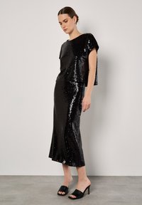 Zwart pailletten top en rok set met een ontspannen pasvorm, met een bootnek, korte mouwen en een uitlopende zoom, gecombineerd met zwarte muilen.