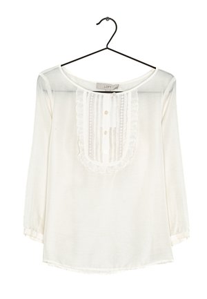 Blusa bianca a maniche lunghe realizzata in tessuto leggero. Presenta una parte anteriore con volant, chiusura con bottoni e scollatura rotonda. Tessuto pulito e liscio.