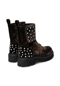 Stivaletti alla caviglia in velluto marrone con texture ornate, impreziositi da borchie bianche sui lati e sul retro. Suola spessa in gomma nera.