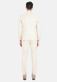 Abito beige con giacca su misura e pantaloni slim-fit, realizzati in tessuto testurizzato, con dettagli di cucitura sottili e spacco posteriore.