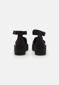Espadrilles noires en toile avec des brides à la cheville, semelles en jute tressé et talon compensé bas. Design simple avec une texture lisse et un minimum de détails.