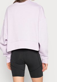 Lila kort sweatshirt med sänkta axlar och texturerat tyg; matchad med figurnära svarta cykelshorts med sömdetaljer.