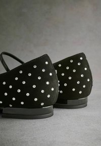 Scarpe in suede nere con tacco arrotondato, adornate con strass trasparenti disposti in un motivo sparso sul retro per un dettaglio decorativo.