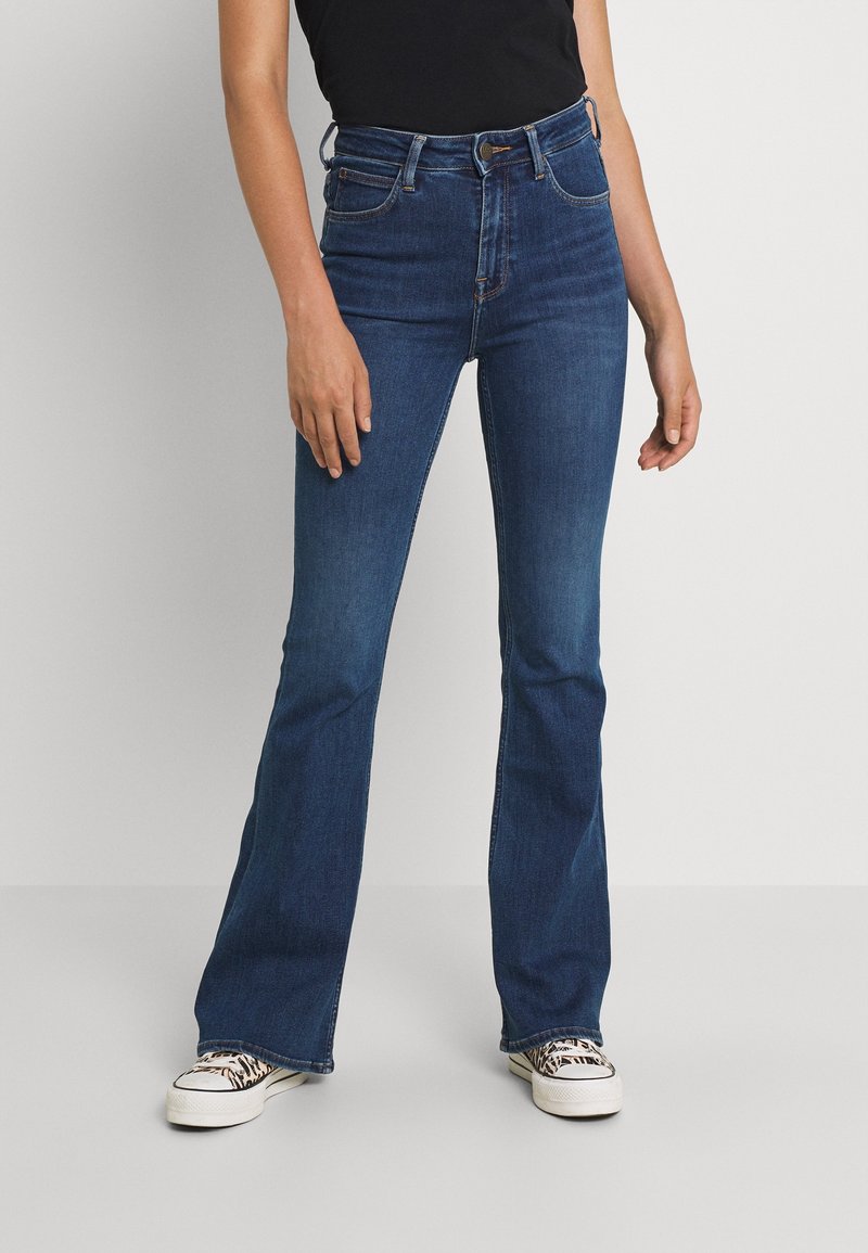 Mörkblå högmidjade utsvängda jeans i denim, med fem fickor och bälteshål. Kombineras med vita sneakers.