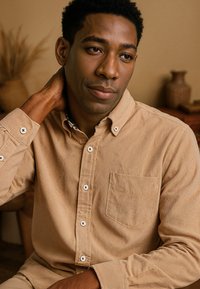 Taupe corduroy shirt met witte knopen, button-down kraag en borstzak. De stof heeft een geribbelde textuur en een lichte glans.