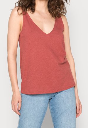 Czerwona bawełniana koszulka na ramiączkach z głębokim dekoltem w kształcie litery V, luźnym krojem i zaokrąglonym dołem. Noszona z jasnoniebieskimi dżinsami, prezentująca casualowy styl.