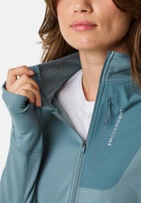 Light blue zip-up jacket with a textured interior, featuring a high collar, thumbholes, and the logo "SWEDEMOUNT" on the chest.