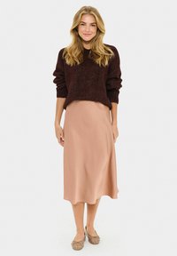 Maroon knit sweater with ribbed cuffs over a blush satin midi skirt. Brown embellished flats. Smooth textures, relaxed fit, and simple design.