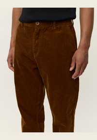Bruine corduroy broek met verticale ribbels, voorzien van een knoopsluiting en zijzakken. Zachte textuur, rechte pasvorm en geen zichtbare patronen.