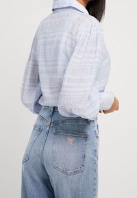 Lichtblauwe gestreepte blouse met poffende mouwen, gecombineerd met hooggetailleerde lichtdenim jeans. De blouse heeft een gestructureerde stof en een knoopmanchet.