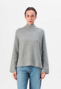 Grå stripete strikkegenser med høy hals, løse ermer og avslappet passform, kombinert med lyseblå jeans.