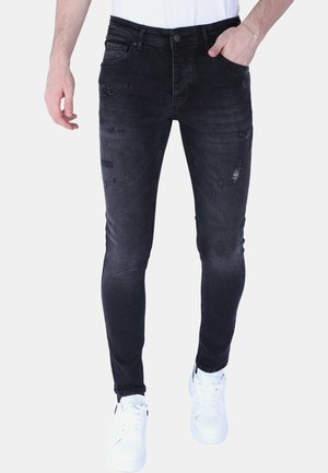 Zwarte skinny jeans met vervaagde gedeelten en versleten details, uitgevoerd in een klassiek ontwerp met vijf zakken. Draagt witte sneakers.