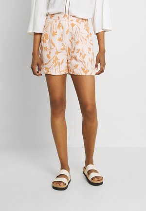 Shorts blancs avec un motif floral orange, taille ajustée et coupe décontractée. Associés à des sandales blanches avec deux larges sangles et une semelle en liège.