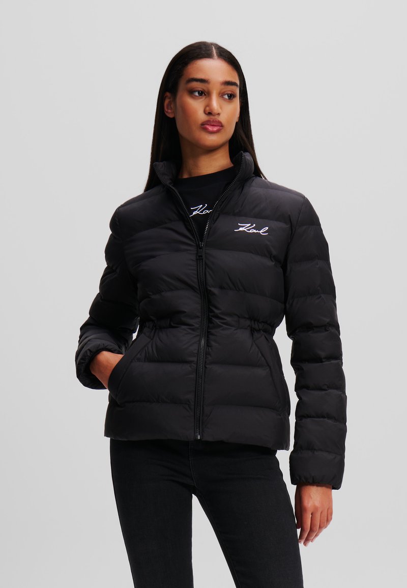 Schwarze wattierte Jacke mit Reißverschluss, hohem Kragen und elastischem Bund. Verfügt über ein gesticktes Logo auf der Brust und seitliche Taschen.