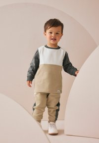 Langærmet top i hvid og beige med grå ærmer; matchende beige bukser med grå accenter; båret med hvide sneakers; blødt materiale.