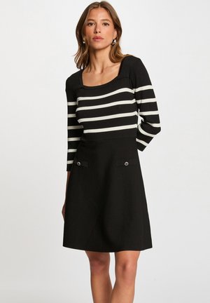 Robe noire avec corsage ajusté rayé et manches trois-quarts. Dotée d'un décolleté carré et de deux poches avant avec des accents métalliques.