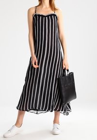 Robe sans manches à rayures noires et blanches avec un décolleté à volants, accompagnée d'un sac à main noir et de chaussures slip-on blanches.