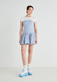 Vestido de ganga azul e branco com corpete ajustado, saia evasê e mangas curtas brancas; combinado com sapatos plataforma azuis chunky.