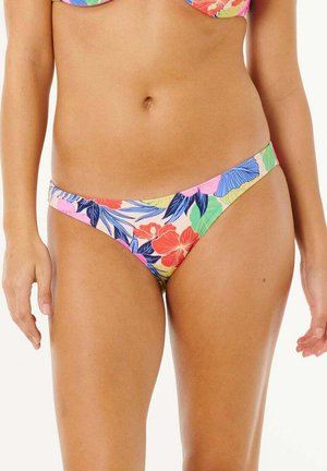 Femme portant un bas de bikini floral coloré avec des feuilles bleues, roses, rouges et vertes, debout les bras détendus le long du corps.